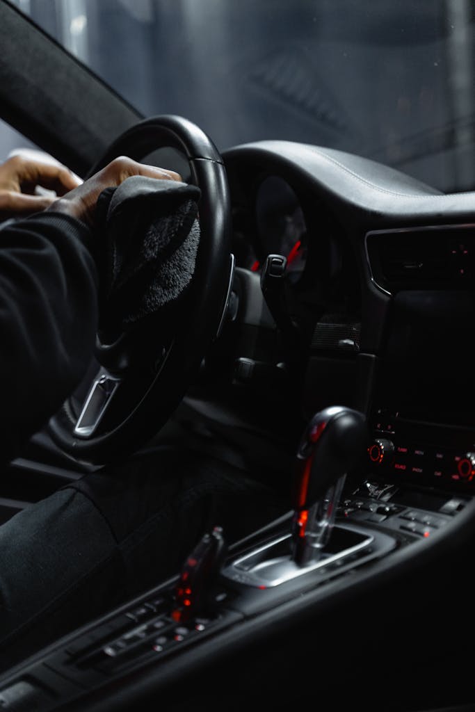 How Does Florida’s Salty Air Affect My Car’s Paint and Interior? (Central Florida Edition) Close-up of a person cleaning a car's dashboard and steering wheel, focused on interior maintenance.