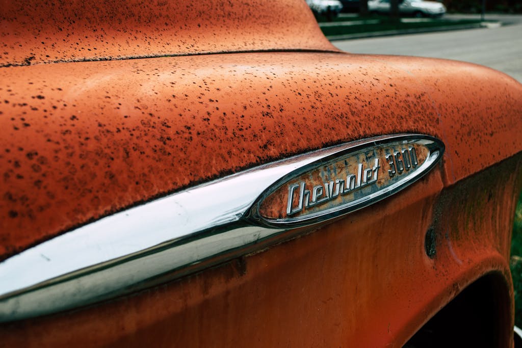 How Does Florida’s Salty Air Affect My Car’s Paint and Interior? (Central Florida Edition) Close-up of a vintage Chevrolet 3600 emblem on a rusty orange truck outdoors.